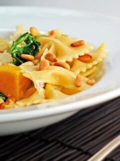 A bowl of pasta with squash, spinach, and pine nuts.