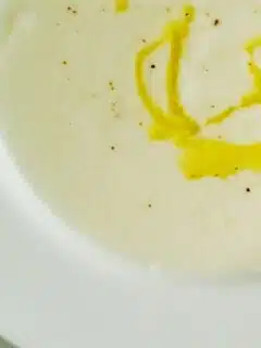 This is a bowl of cauliflower soup with a drizzle of yellow sauce on top.