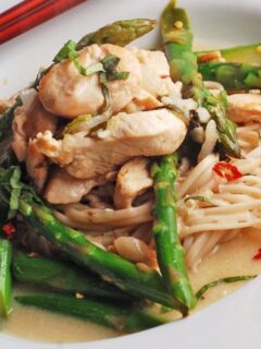 Thai inspired Chicken and asparagus sit atop a white plate of noodles.