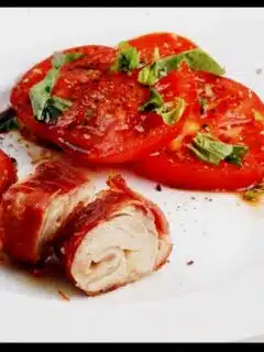 A plate with tomatoes and pork wrapped in bacon.