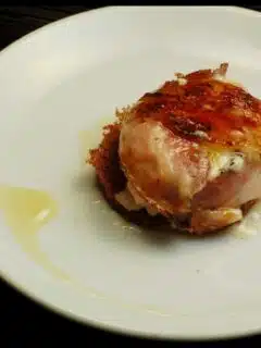 A white plate with a piece of meat topped with pancetta.