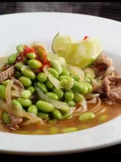 A bowl of noodles with beef and peas.