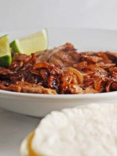A bowl of pulled pork with lime wedges and tortillas, perfect for a quick weeknight dinner.