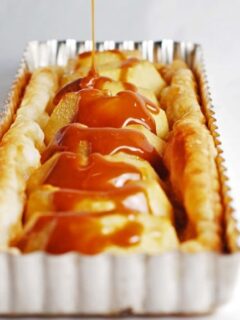 A Parisian apple tartlet is being drizzled with burnt salted caramel sauce in a pan.