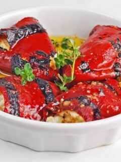 Grilled red peppers in a white bowl, stuffed with goat cheese.