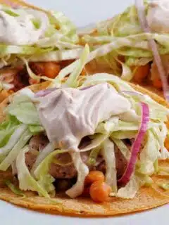 Three snapper tacos with slaw and sour cream on a plate.