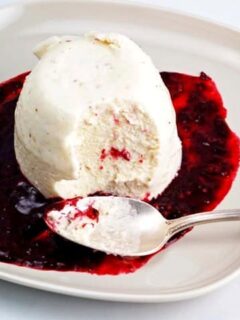 A white plate with a scoop of ice cream topped with raspberry sauce.