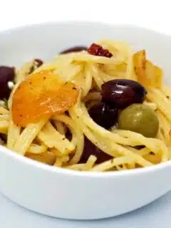 A white bowl with pasta and olives.