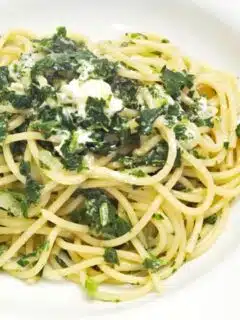 A plate of spaghetti with spinach and feta cheese is served.