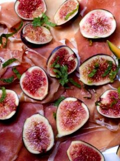 Enjoy figs and prosciutto on a white plate during Sunday dinner with friends.