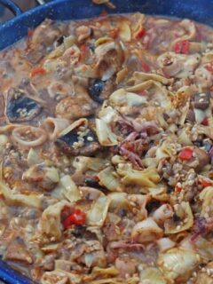 A large pot of Paella with Mushrooms simmering over an open fire.