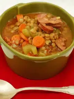 A bowl of chorizo and lentil soup with meat and vegetables on a red napkin.