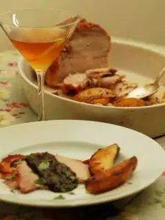 A plate of pork tenderloin in a port-prune sauce, potatoes and a glass of wine.