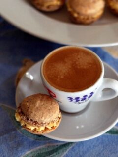 A cup of coffee and a plate of macarons, including Tonka Bean and Passion Fruit flavors.