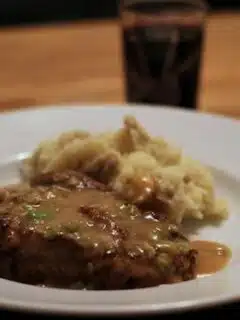 A plate of Chicken Fried Steak with Green Garlic Gravy and mashed potatoes on the table.