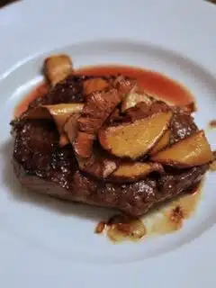 A steak with sauteed chanterelles and sauce on a plate.