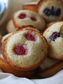 Berry Financiers with raspberries and blueberries on a white cloth.