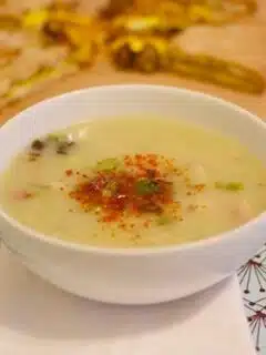 A bowl of potato and leek soup with bread and wine on a table.
