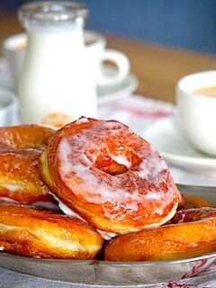 A plate of cardamom doughnuts on a table next to a cup of coffee.