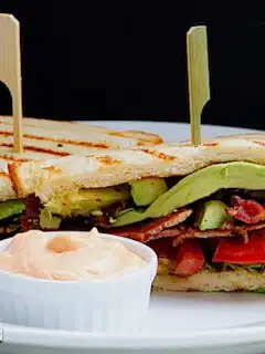 A Spicy B.L.A.T sandwich with bacon and avocado on a white plate.