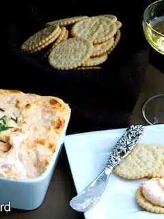 A plate with crackers and a glass of wine, perfect for enjoying the spicy hot crab dip.