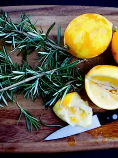 Slices of lemon and sprigs of rosemary on a cutting board.