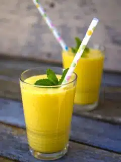 Two glasses of mango lassi on a wooden table.
