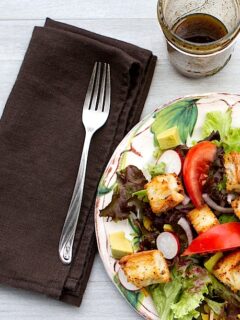A plate of salad with homemade croutons on a wooden table.
