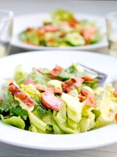 A salad with bacon and avocado on a white plate, topped with creamy Asian avocado dressing.