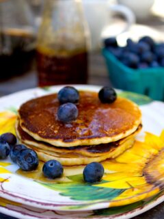 A stack of homemade pancakes on a plate with blueberries.