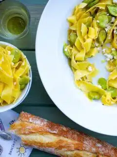 A bowl of pasta with green beans and bread on the table.