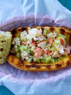 A homemade lobster roll topped with a buterry lobster salad and served with corn on the cob.