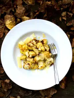 A white plate with roasted cauliflower and cheese on it.