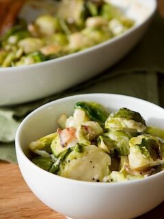 Brussels sprouts in a white bowl on a wooden table, perfect for Brussels Sprout Gratin.
