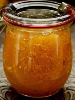 A jar of orange marmalade, infused with bergamot and vanilla bean, sitting on a table.