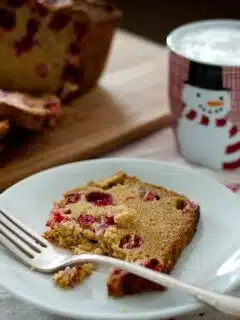 Cardamon cranberry bread on a plate with a cup of coffee.