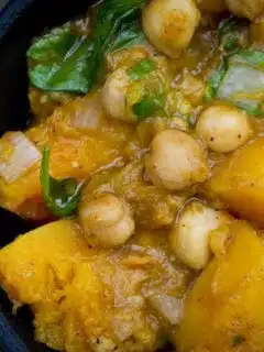 A bowl of curry with chickpeas and spinach mixed in.