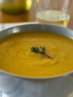 A bowl of butternut squash and pear soup garnished with a sprig of rosemary.