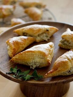 Olive and goat cheese turnovers on a wooden plate with a sprig of thyme.