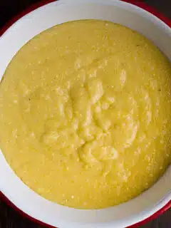 A bowl of yellow polenta taleggio on a wooden table.