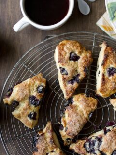 Blueberry scones on a cooling rack alongside a cup of coffee.