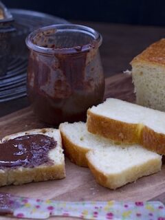 A slice of golden brioche and a jar of jam on a cutting board.