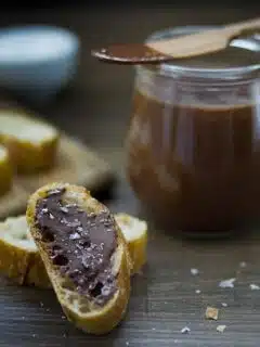 A jar of homemade chocolate spread on a wooden cutting board.