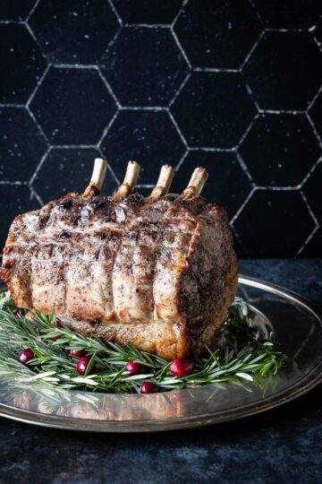 A pork prime rib roast with rosemary and cranberries on a plate.