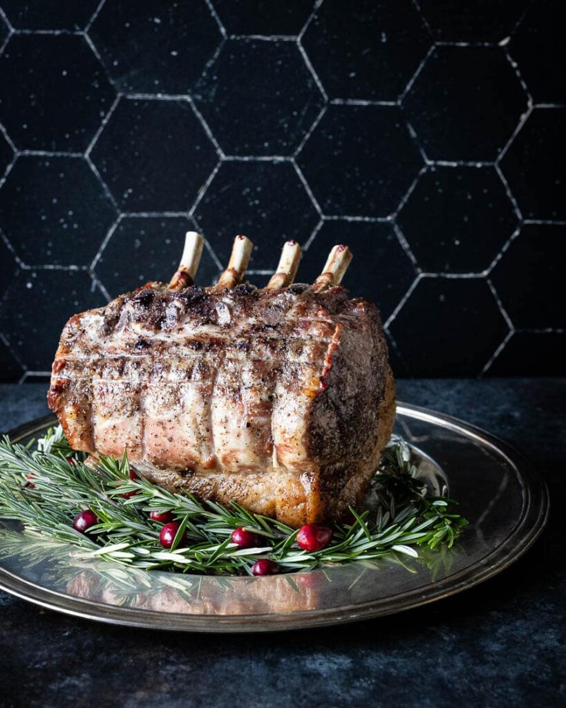 A pork prime rib roast with rosemary and cranberries on a plate.